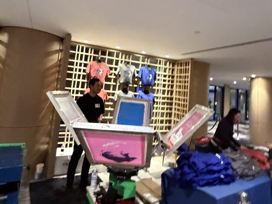 A manual screen-print press loaded with a pink screen at a brand activation