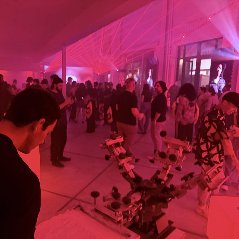 A nighttime event with magenta laser-fan lighting, a crowd, and a live screen-print carousel
